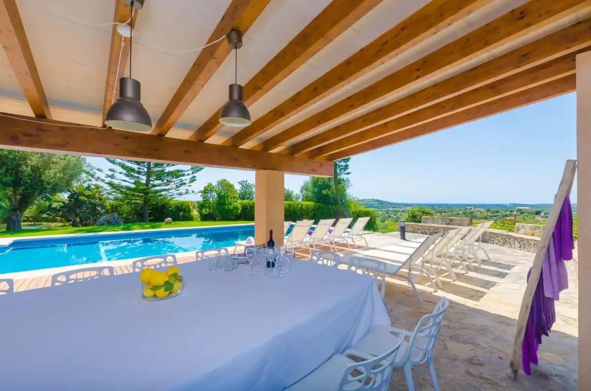 A covered outdoor dining area overlooks a swimming pool and garden.