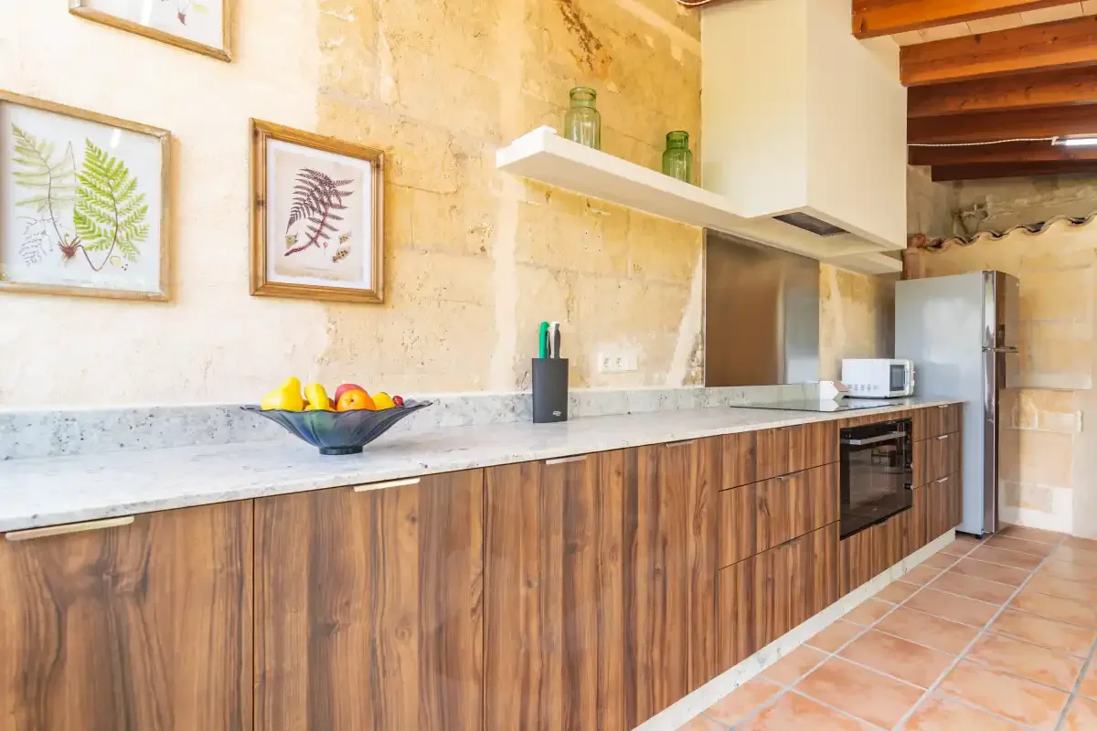 A kitchen with a long counter, wood cabinetry, and a bowl of fruit.