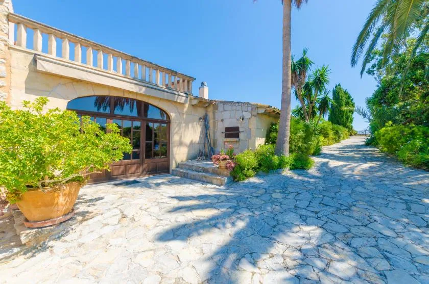 A stone-paved outdoor path runs beside a building entrance and tropical greenery.