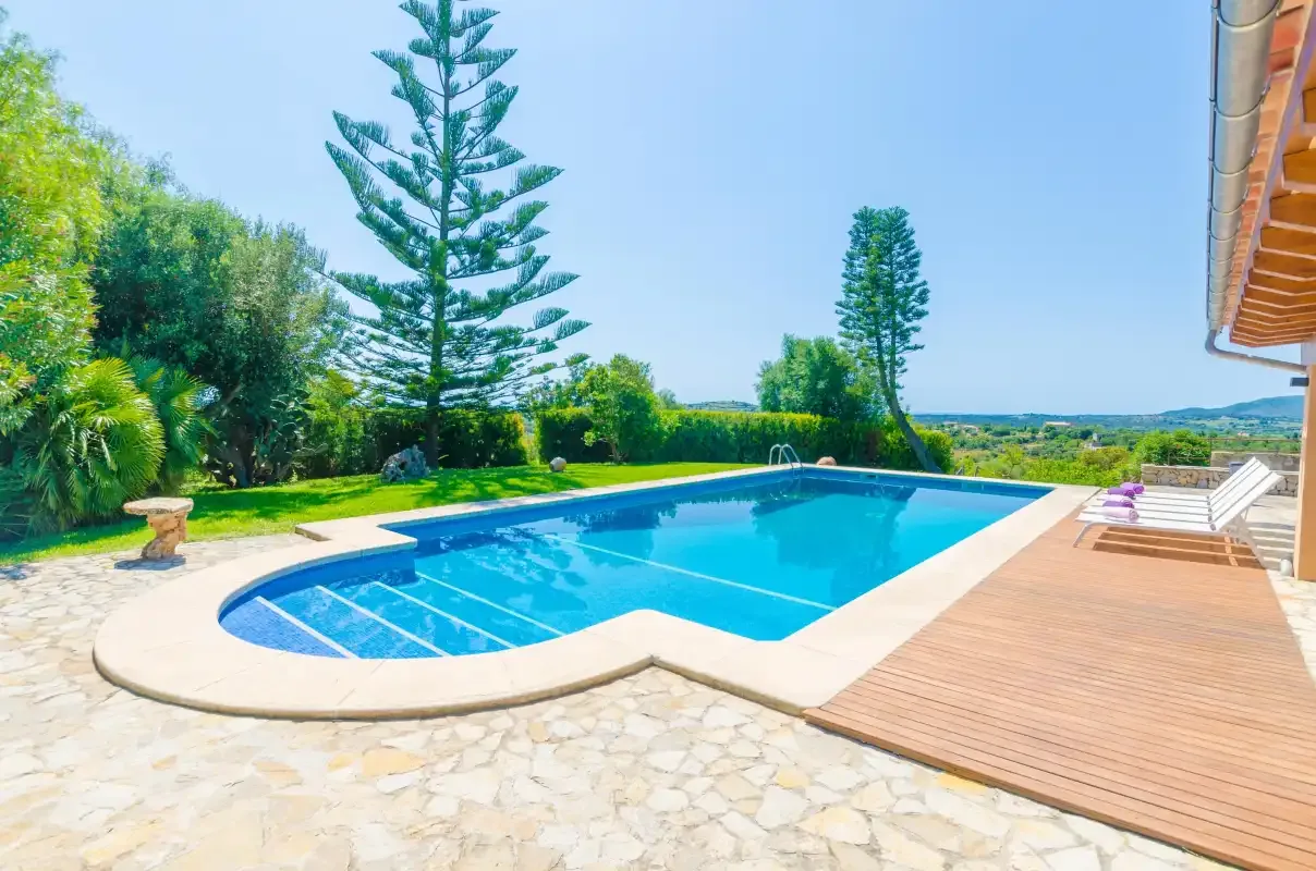 An outdoor swimming pool beside a wooden deck, with greenery in the background.