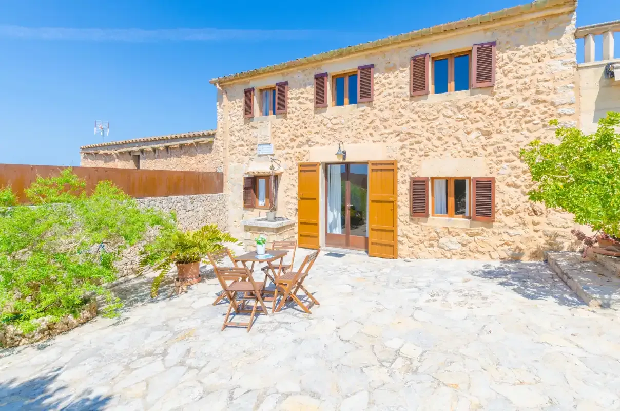 A stone house opens onto a paved courtyard with outdoor seating.