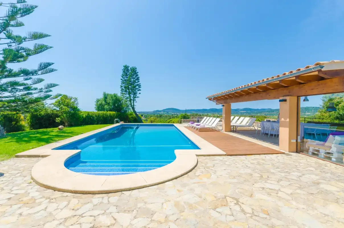An outdoor swimming pool sits beside a covered patio with seating.