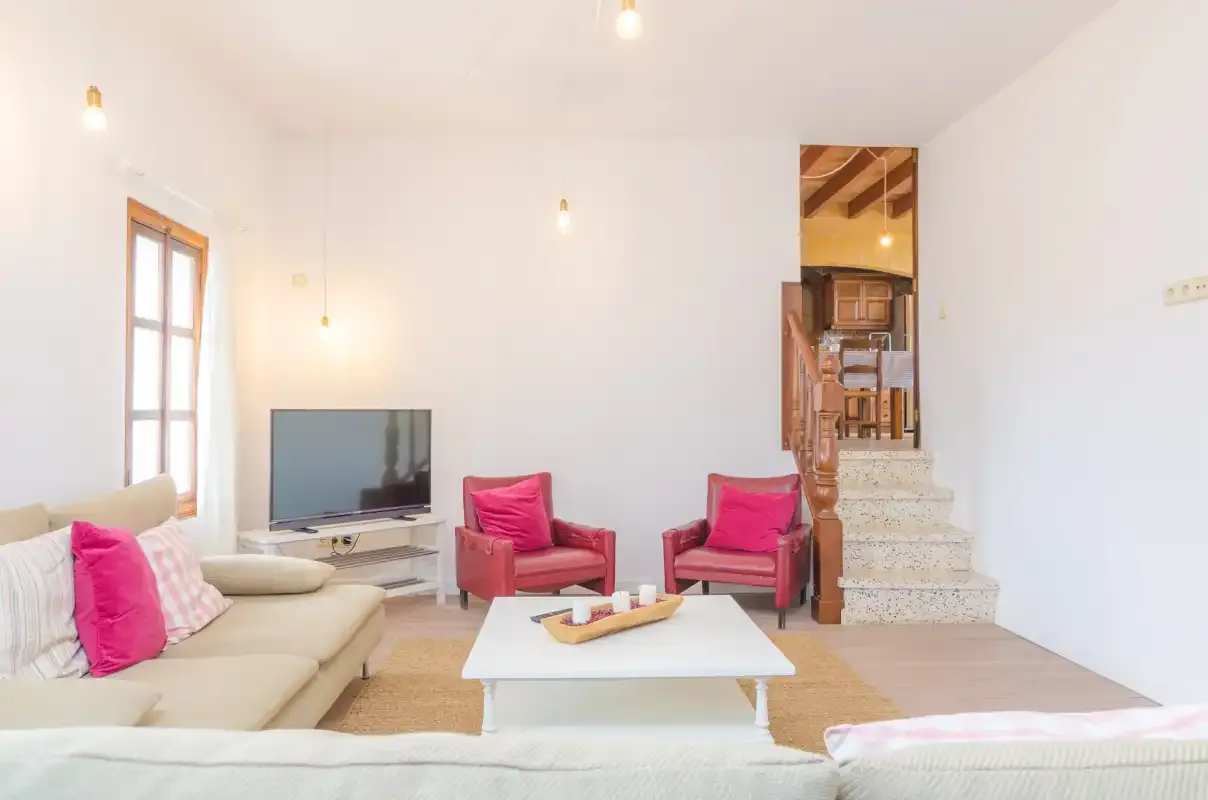 A bright living room with seating, a television, and stairs.