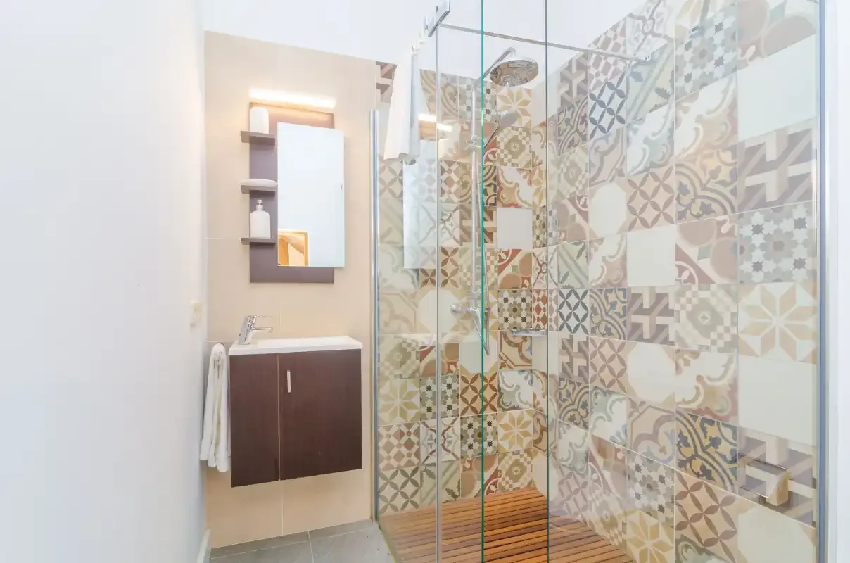 A bathroom with a glass shower and patterned tile walls.