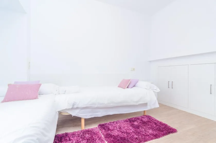 A bright bedroom with a white bed and a pink rug.