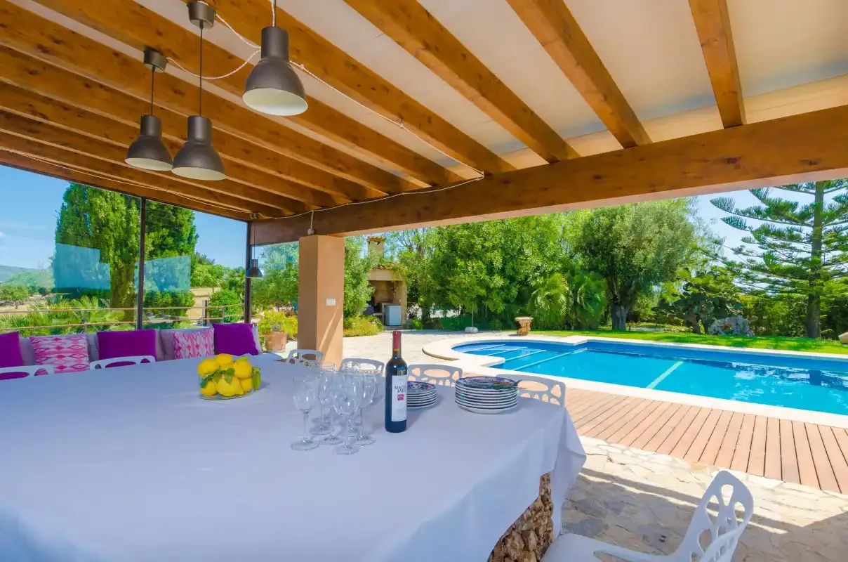 A covered outdoor dining area overlooks a swimming pool and garden.