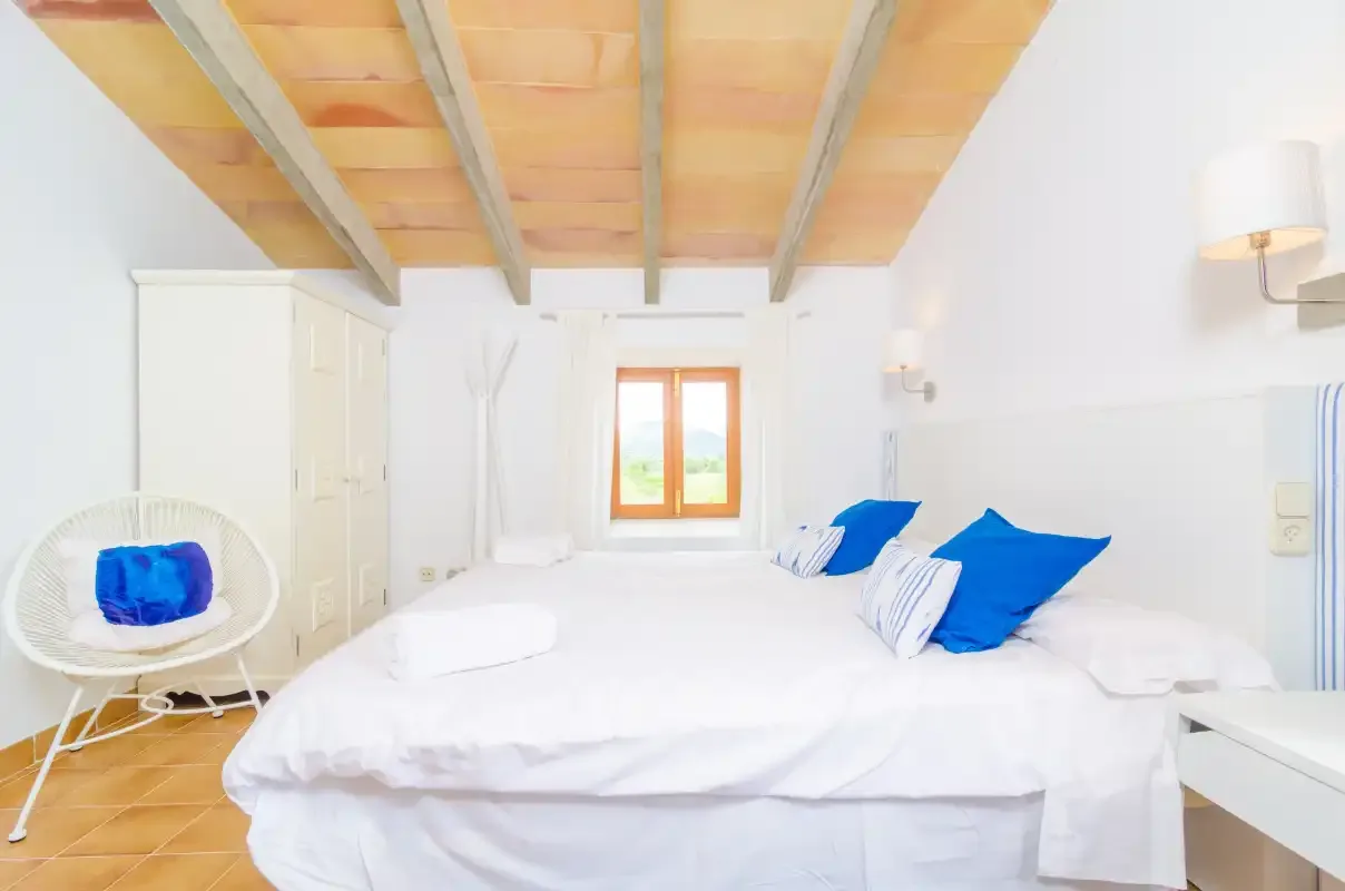 A bright bedroom with white bedding and blue accent pillows.