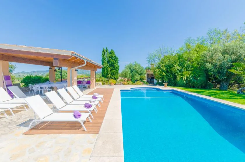 An outdoor swimming pool beside a paved deck with lounge seating and a shaded patio.