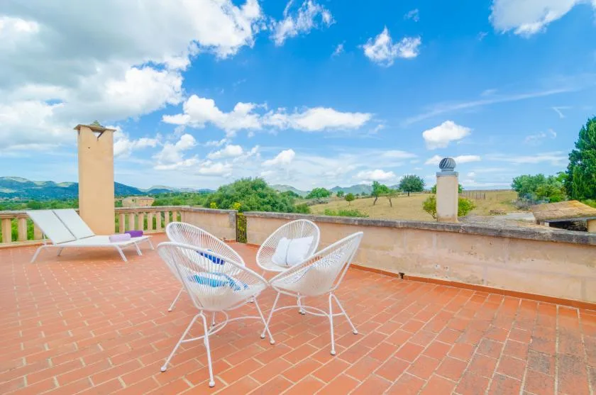 A tiled outdoor terrace has white seating and open countryside views.