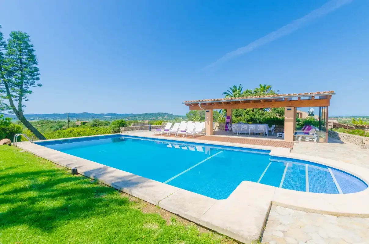 A swimming pool beside a shaded seating area overlooks green countryside.