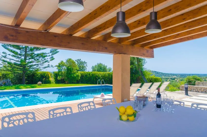 A covered outdoor dining area overlooks a swimming pool and green landscape.