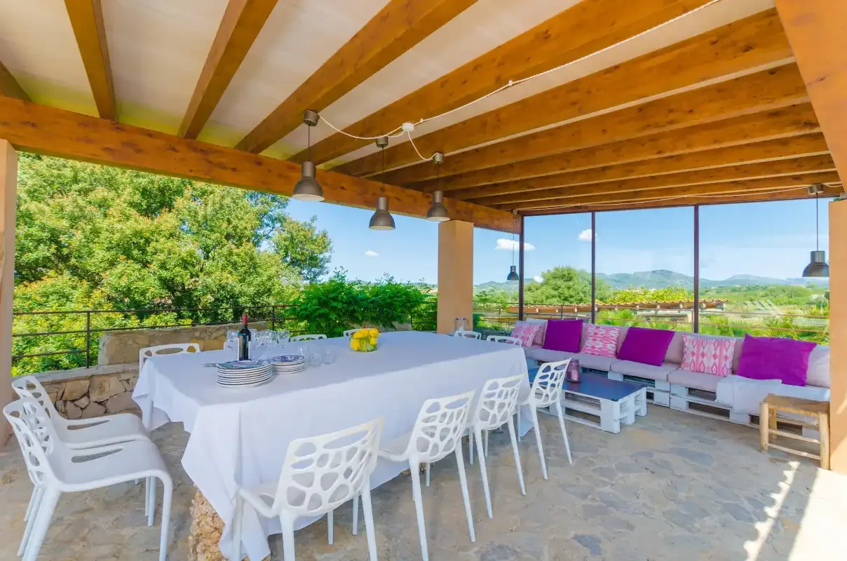 A covered outdoor dining area with a table, seating, and views of greenery.
