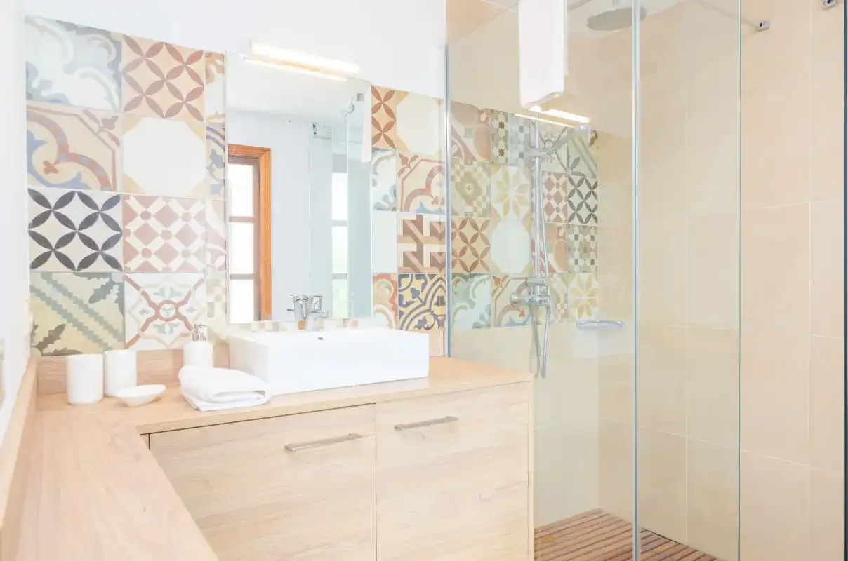 A bright bathroom has a vanity beside a glass shower and patterned tiles.