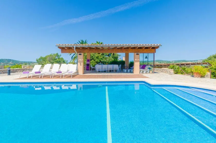 An outdoor swimming pool with a shaded seating area and loungers beside it.