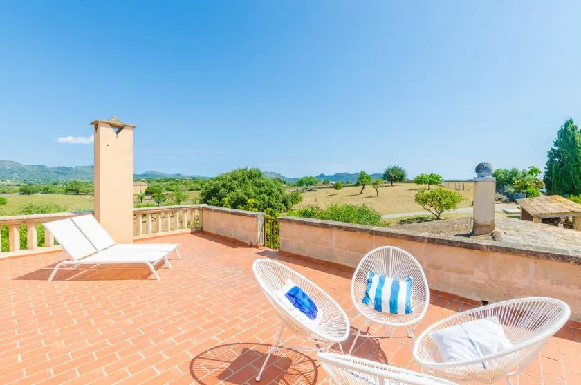 A sunny rooftop terrace with white seating overlooking an open countryside landscape.