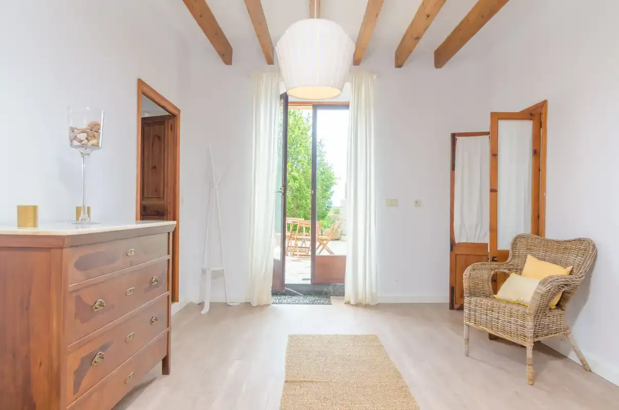 A bright bedroom with a wicker armchair and glass doors opening to a patio.