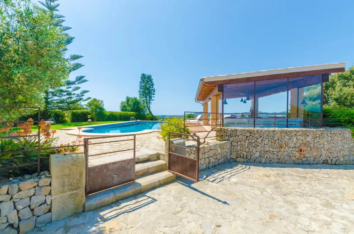 A stone-paved outdoor area leads to a modern glass-fronted building beside a pool.