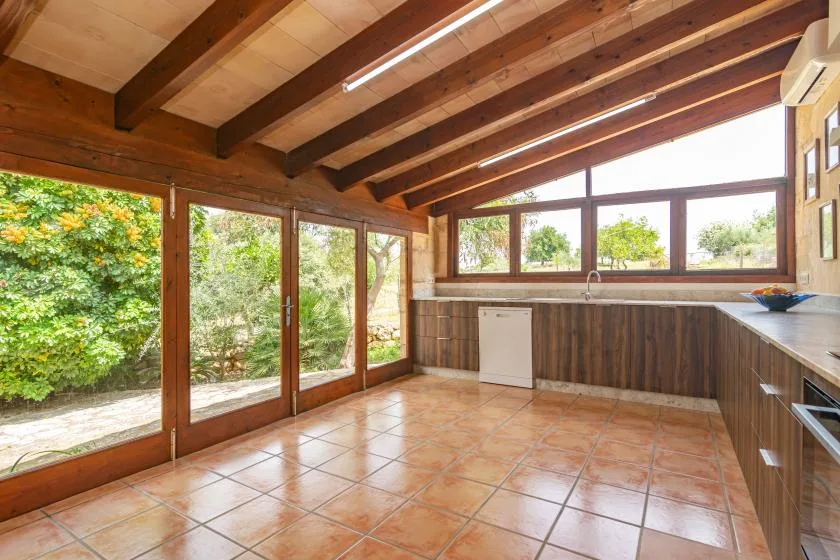 A sunlit kitchen opens onto a leafy garden through large glass doors.