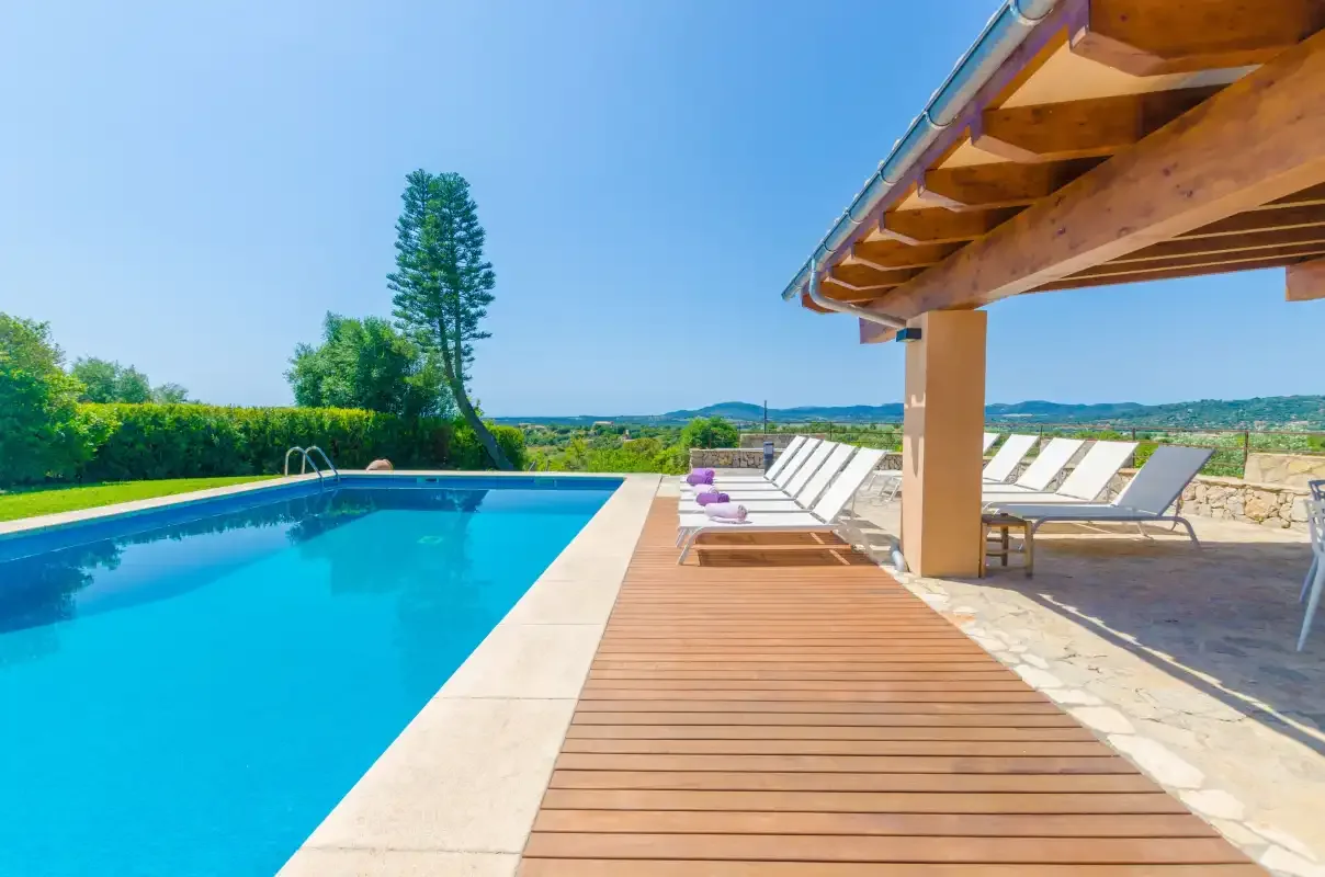 Outdoor pool beside a wooden deck, with loungers beneath a covered patio.
