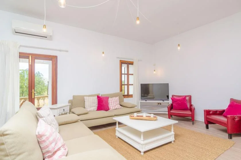 A bright living room with pale seating, a television, and a low coffee table.