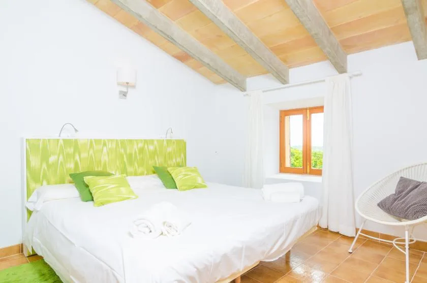 A bright bedroom with a white bed and a window beside it.