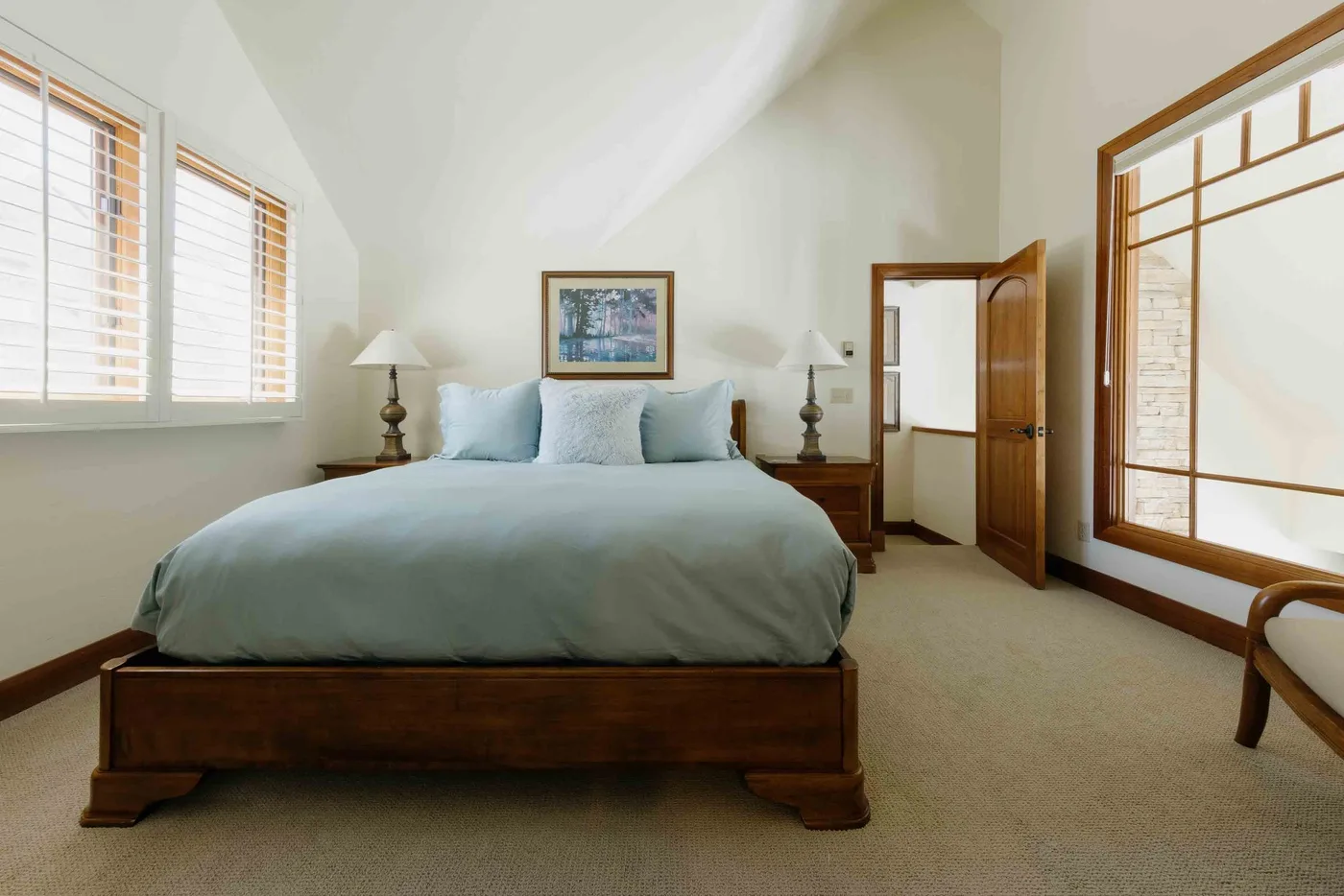 A bright bedroom with a bed, bedside tables, and large windows.