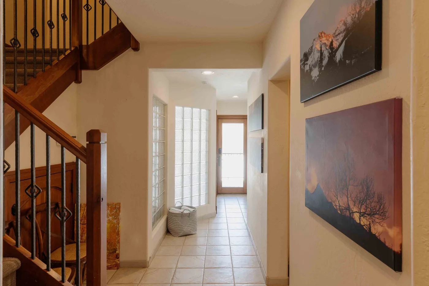 A tiled hallway with a wooden staircase and framed artwork on the wall.