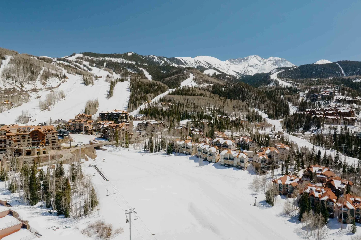 A snow-covered ski resort spreads across a mountain valley beneath a clear blue sky.