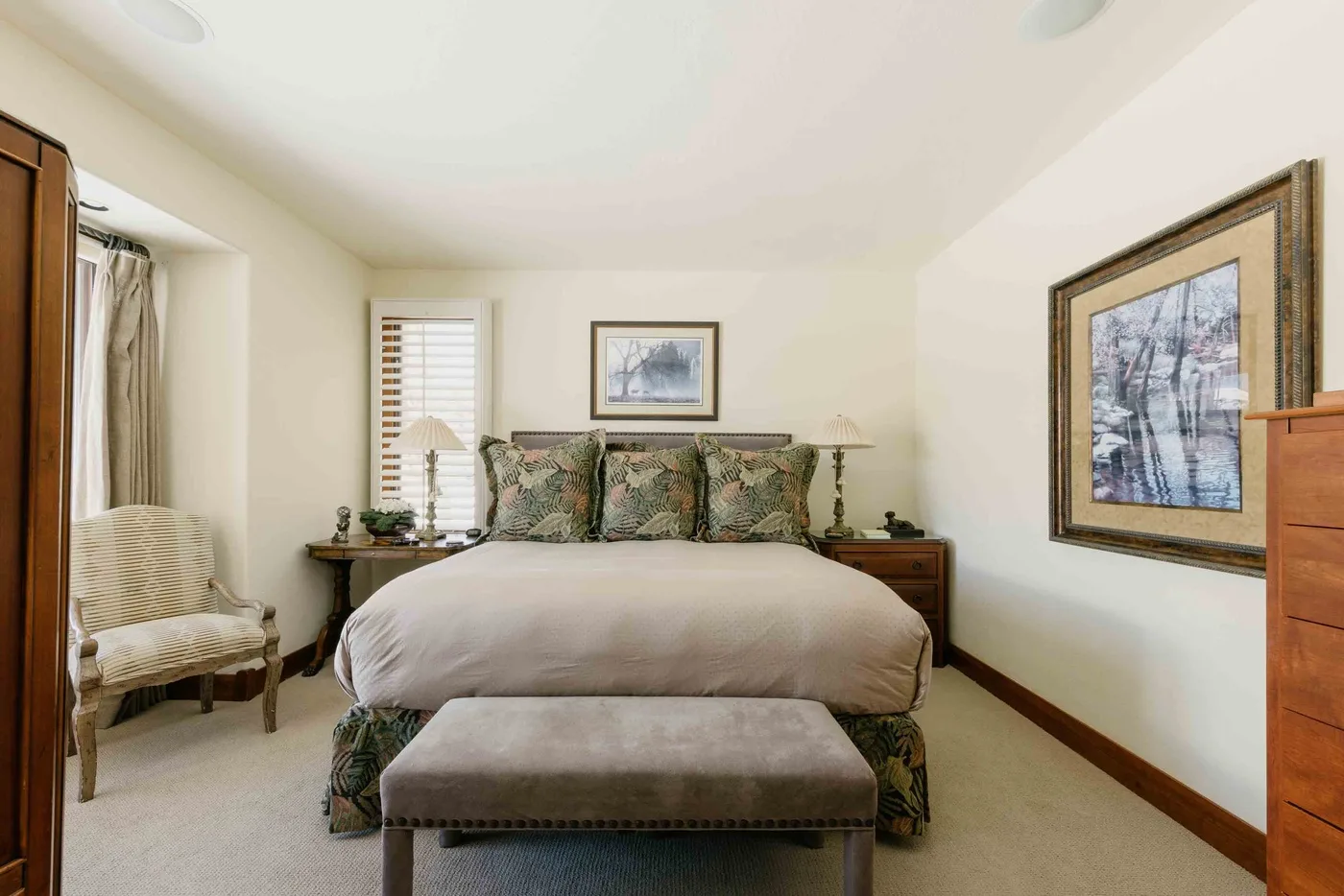 A bedroom with a neatly made bed, a chair, and framed artwork.