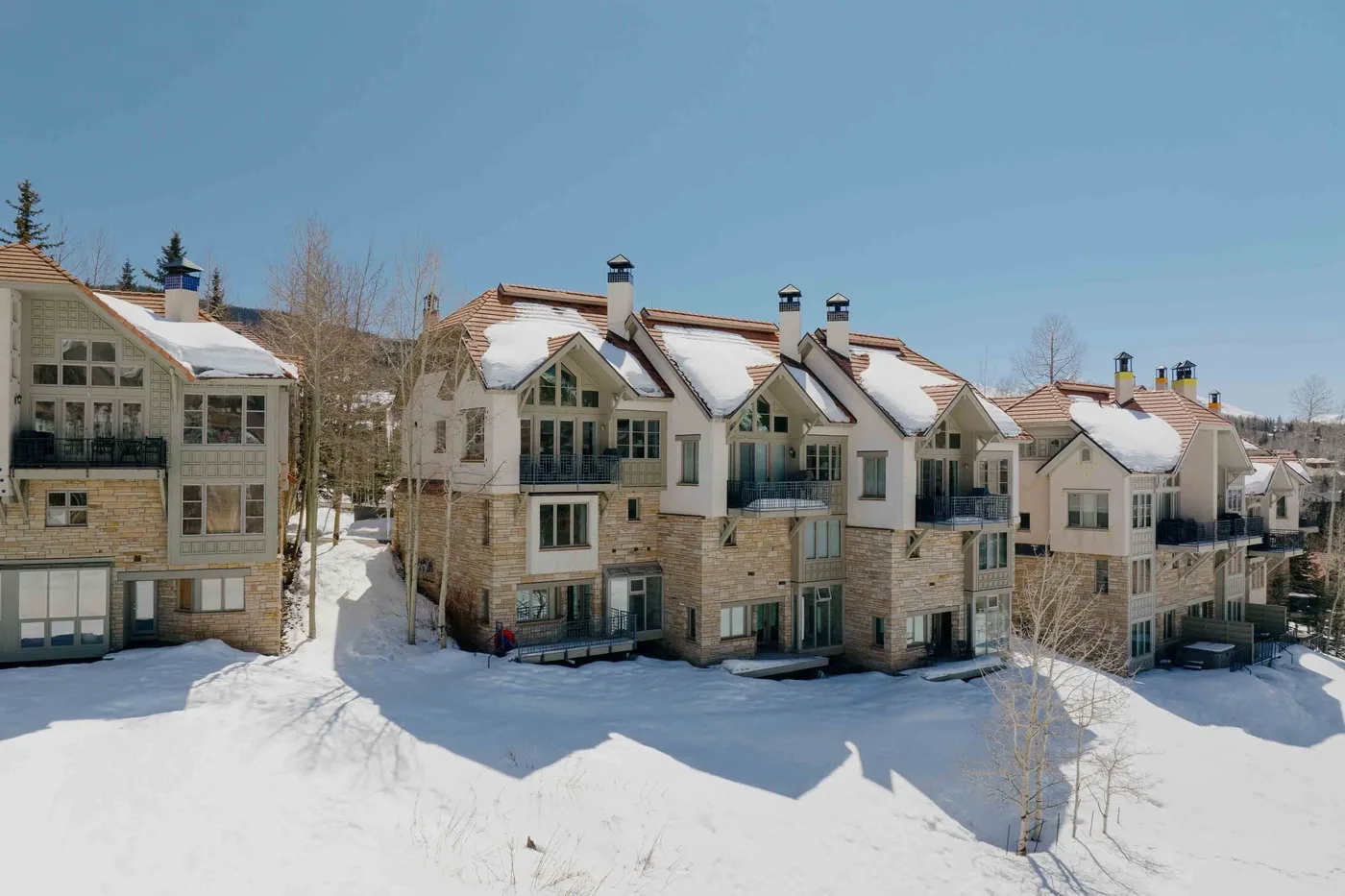 A row of multi-story buildings stands beside a snow-covered slope under a clear sky.