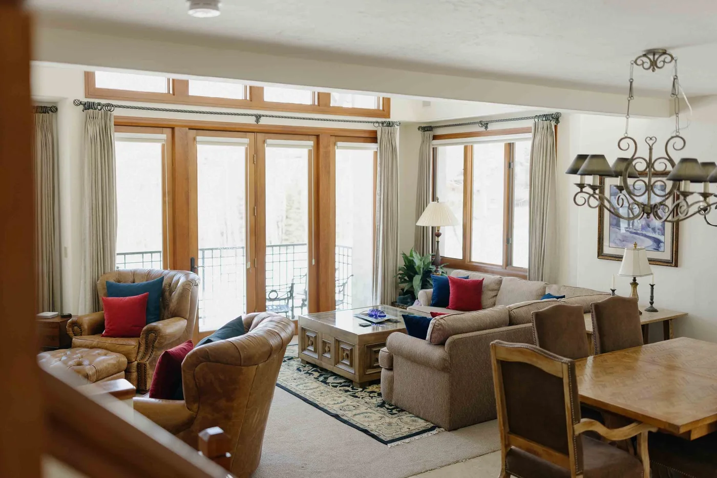 A living room with seating around a coffee table beside tall windows.