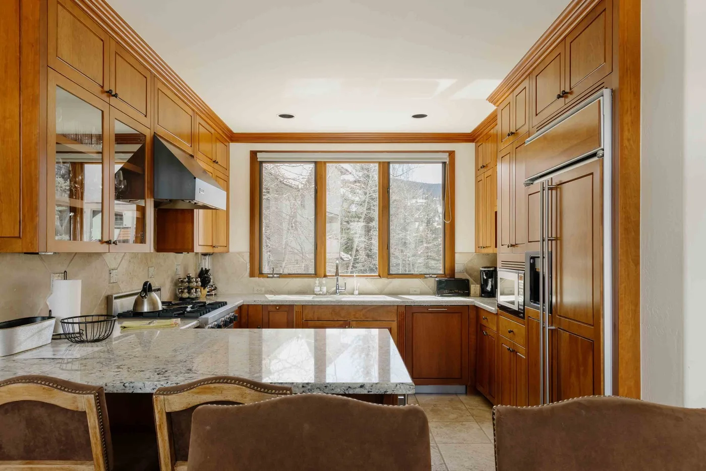 A kitchen with wooden cabinetry, stone counters, and a window over the sink.