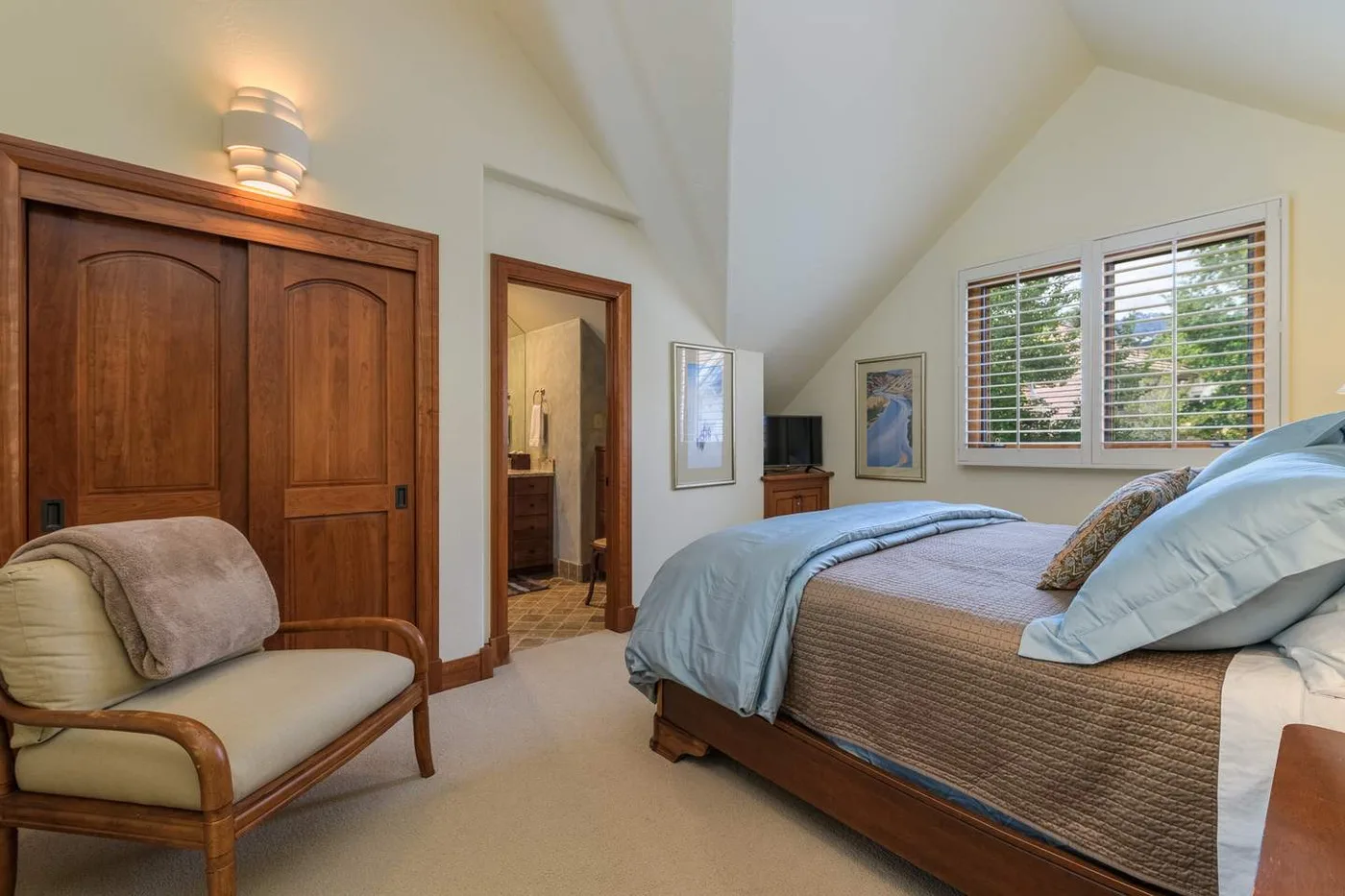 A bright bedroom with a bed, a wooden wardrobe, and a window.