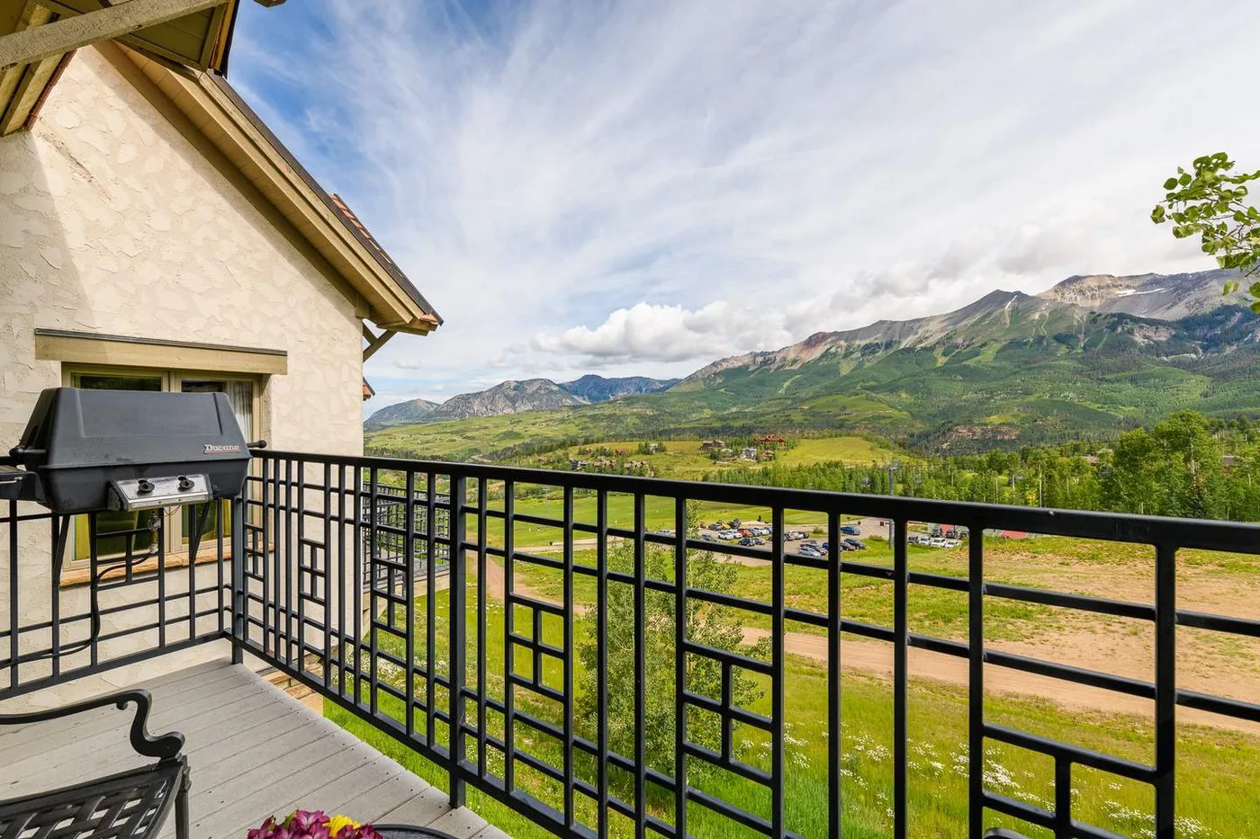 A balcony overlooks a green valley and mountain range, with a grill beside the railing.