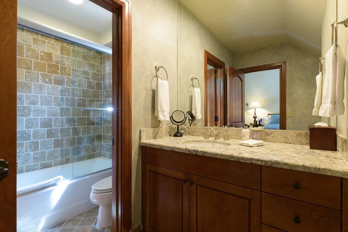 A bathroom vanity with a wide mirror faces a tiled shower and bathtub.
