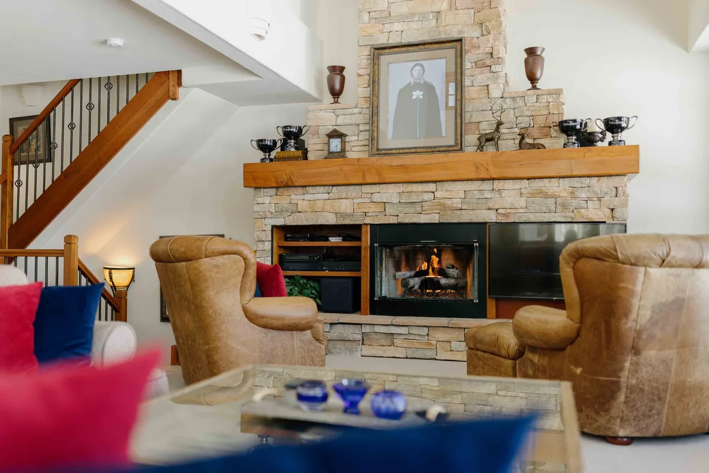A living room with a stone fireplace, seating, and a staircase.