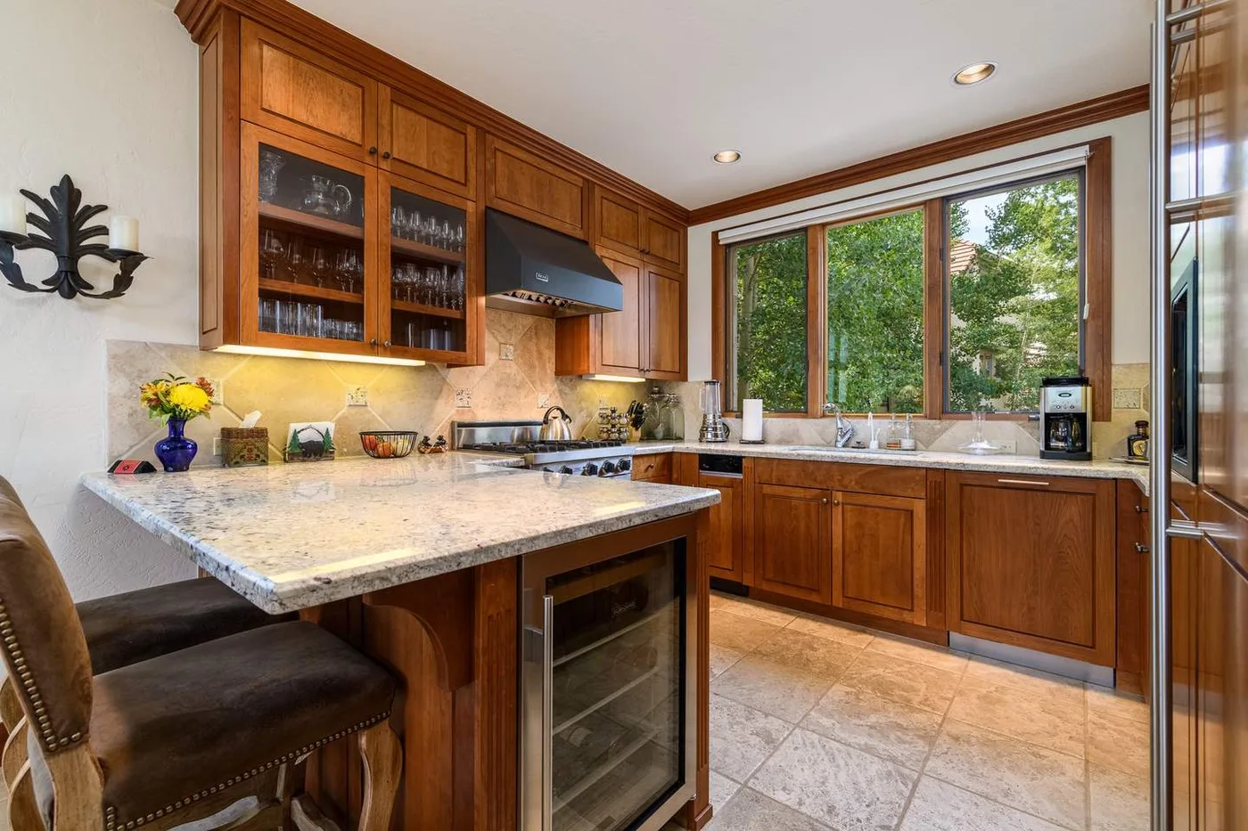 A spacious kitchen with wooden cabinets, a stone island, and a large window.