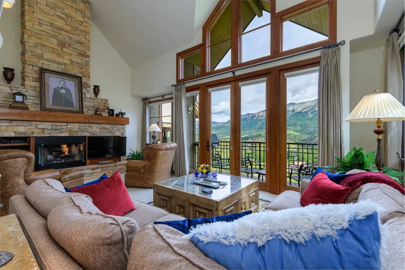 Una sala de estar con chimenea de piedra y ventanales con vistas a un valle montañoso.