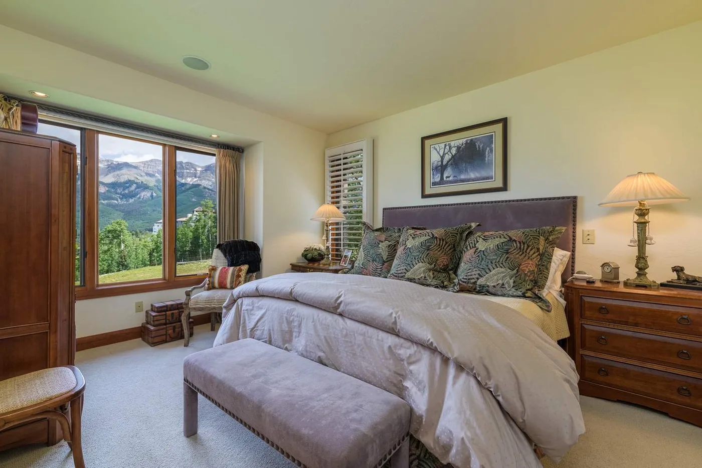 A bedroom with a large bed, bedside tables, and a window overlooking mountain scenery.
