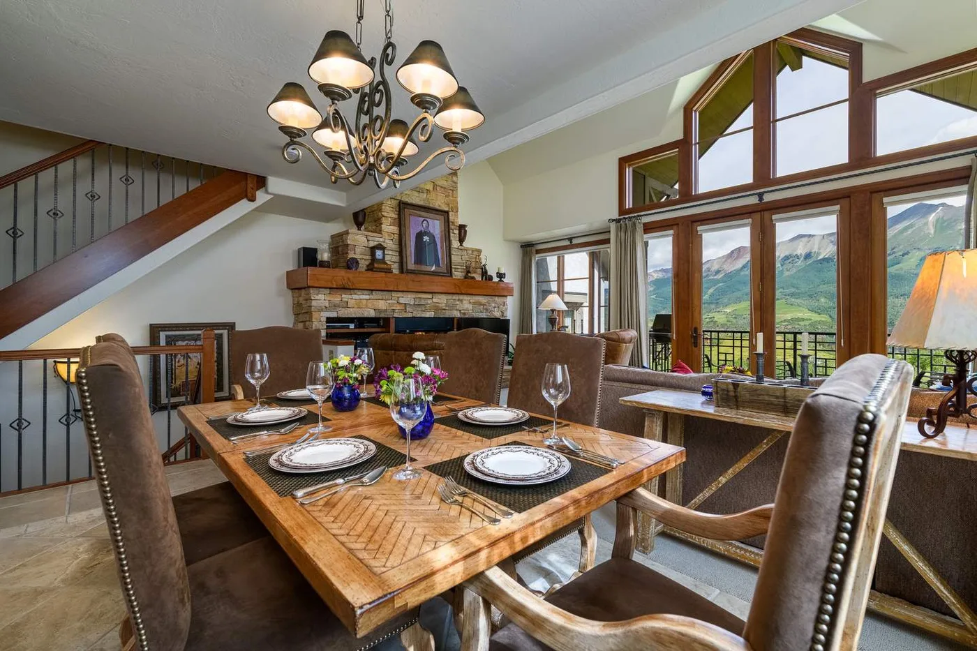 Comedor con una mesa preparada, una chimenea y grandes ventanas con vista a las montañas.