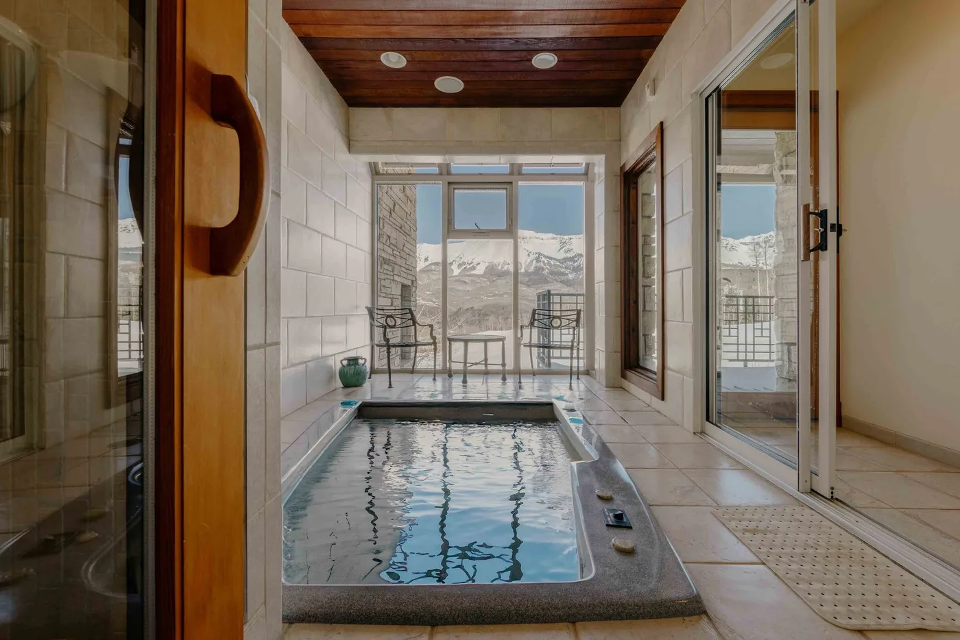 An indoor plunge pool sits beside large windows overlooking a mountain landscape.