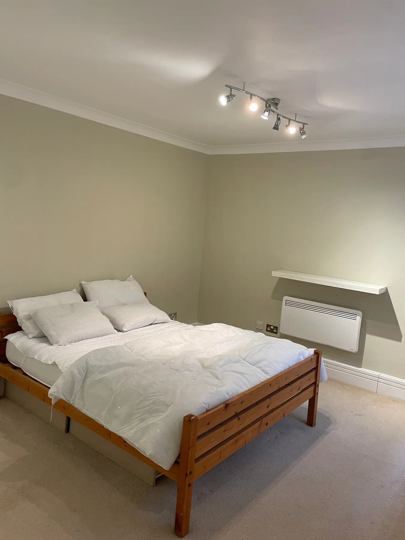 A bedroom with a wooden bed, white bedding, and a wall-mounted heater.