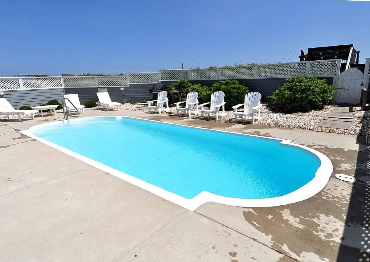 Una piscina al aire libre con sillas blancas junto al borde.