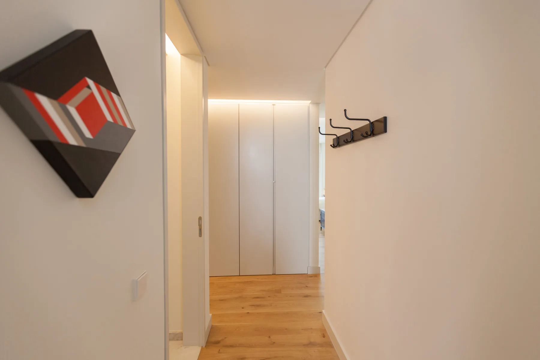 A hallway with wood flooring, wall art, and coat hooks.