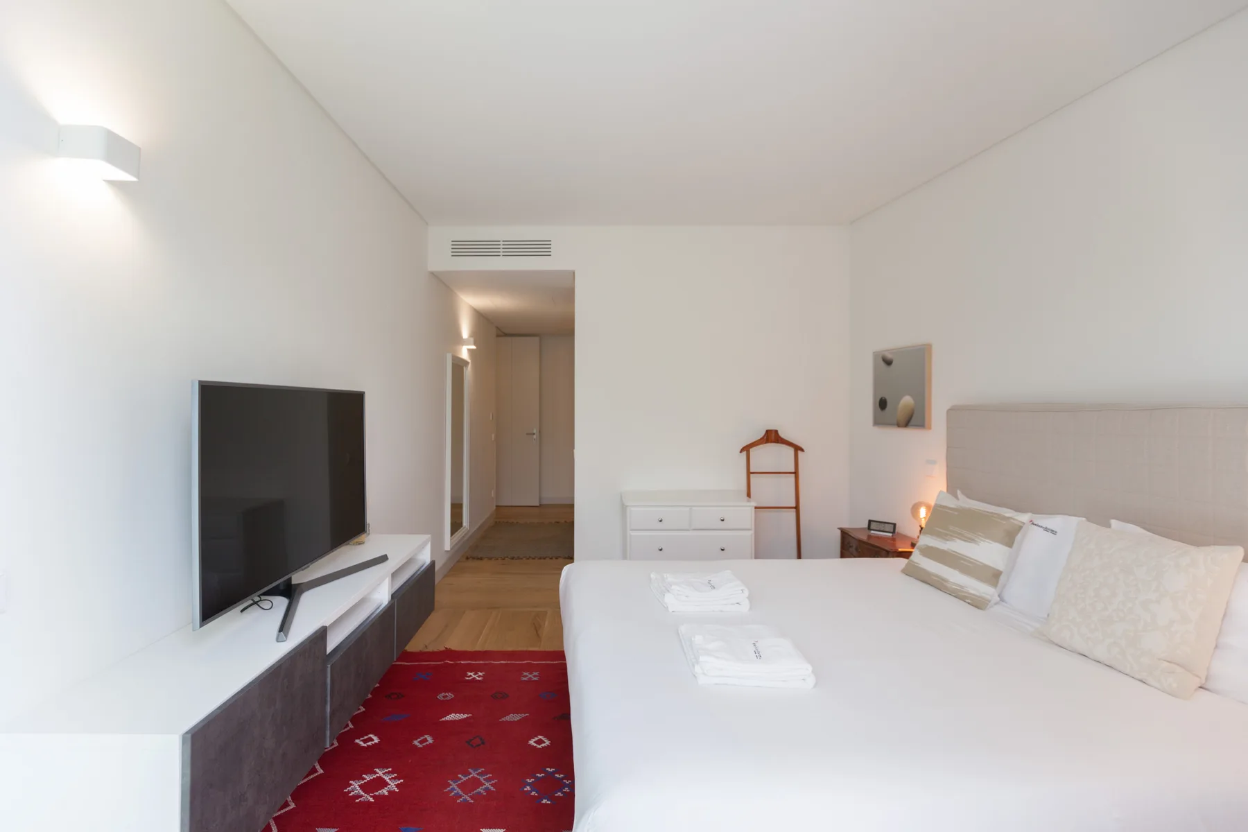 A bright bedroom with a bed, television, and red patterned rug.
