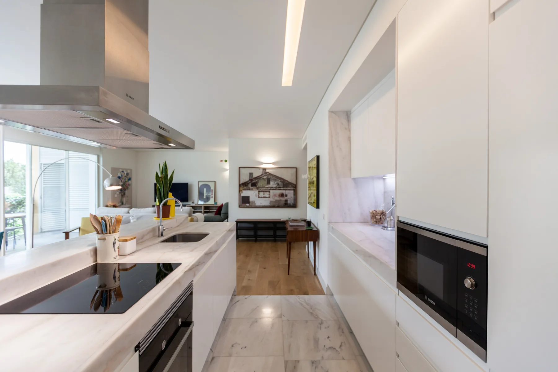 A bright modern kitchen opens onto a dining area, with a long island and built-in appliances.