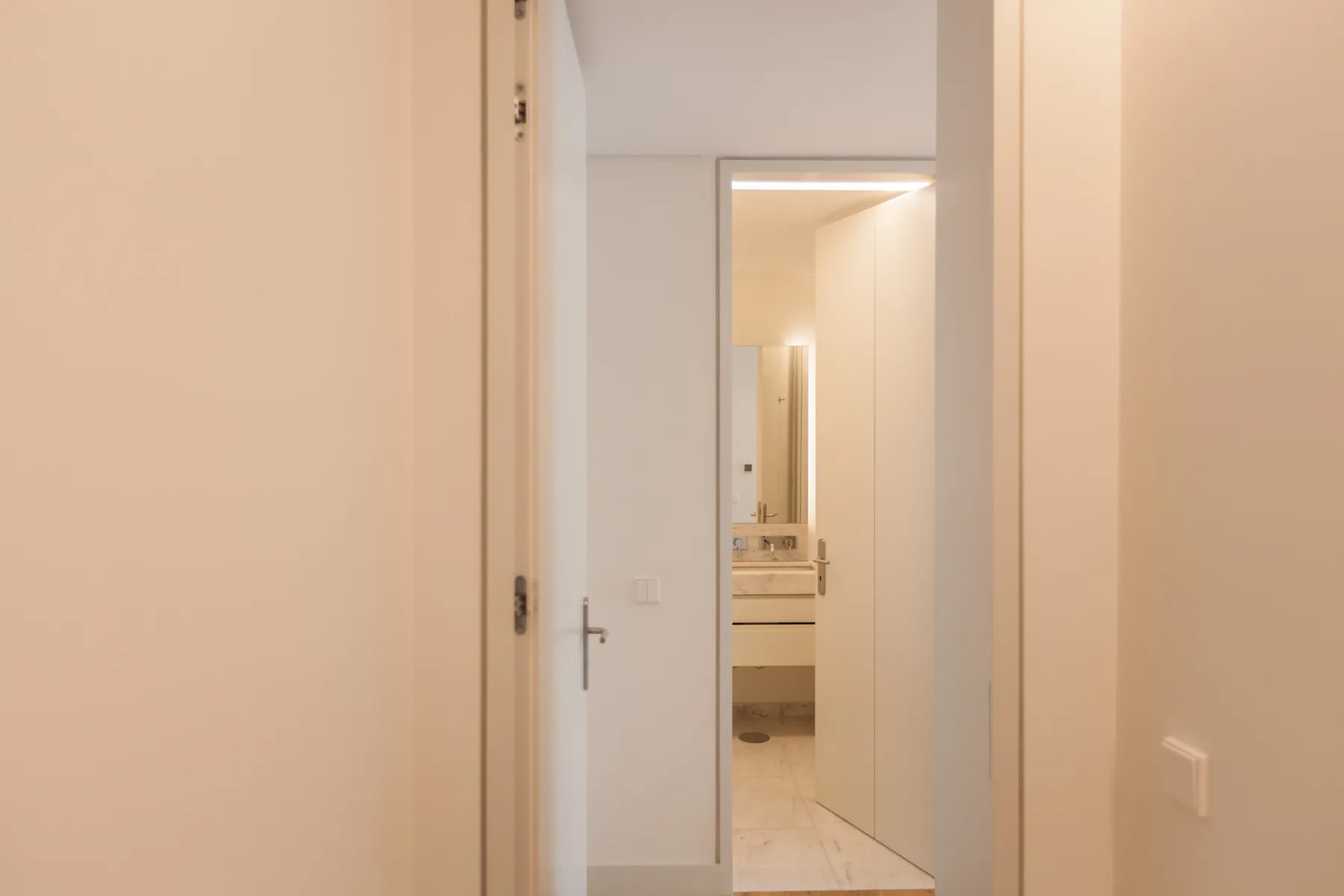 A hallway leads to a bathroom with a visible sink and mirror.