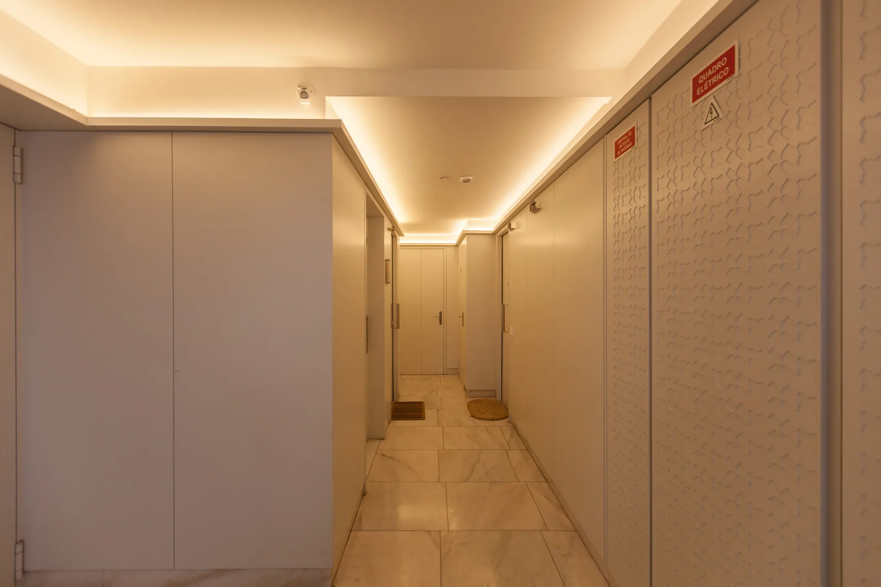 A narrow indoor corridor with tiled flooring and doors along the walls.
