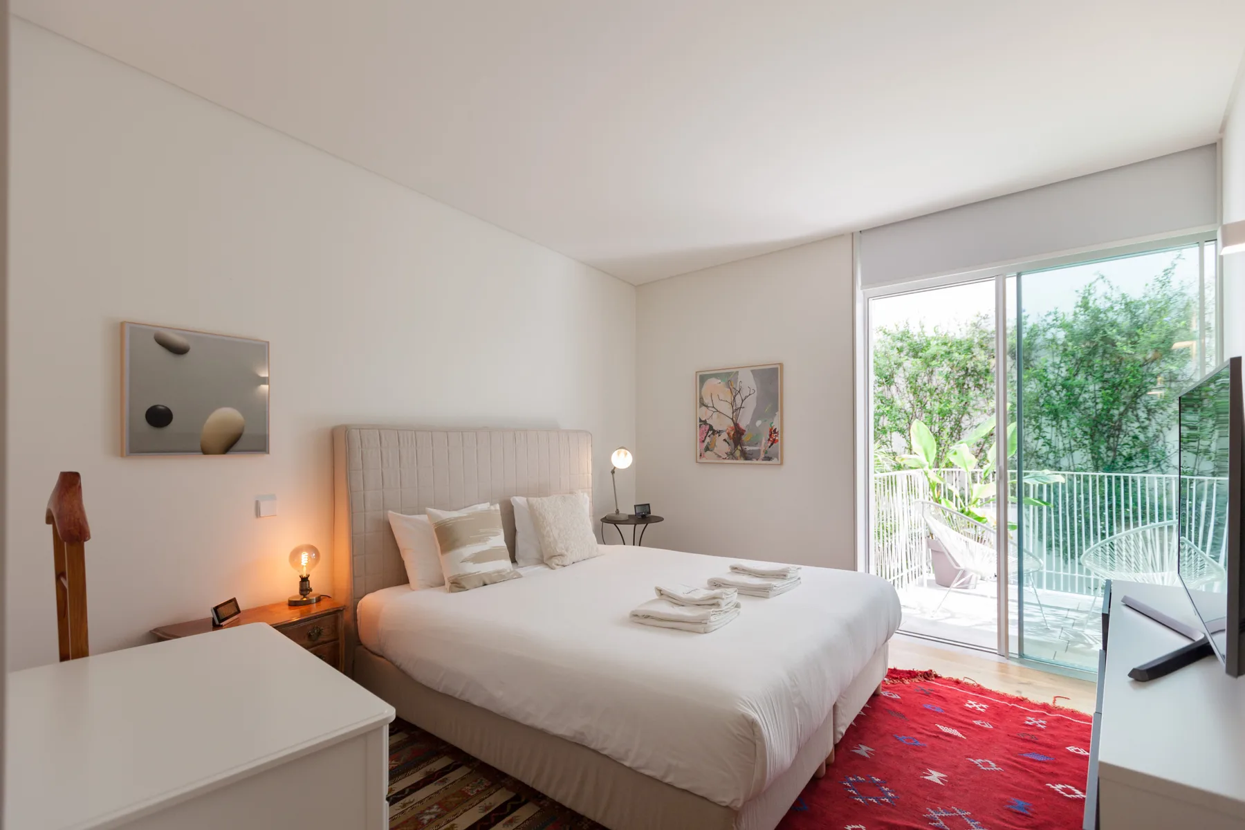 A bedroom with a neatly made bed and sliding glass doors opening onto a balcony.