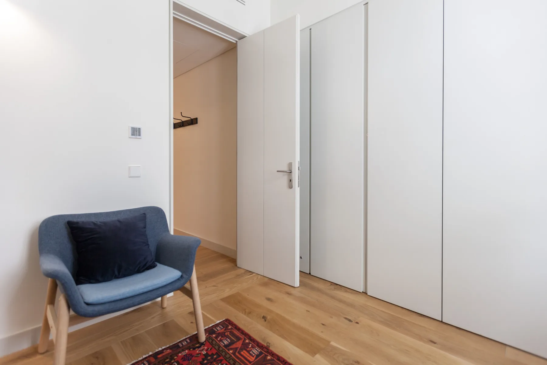A room with a blue chair beside an open doorway and built-in wardrobes.